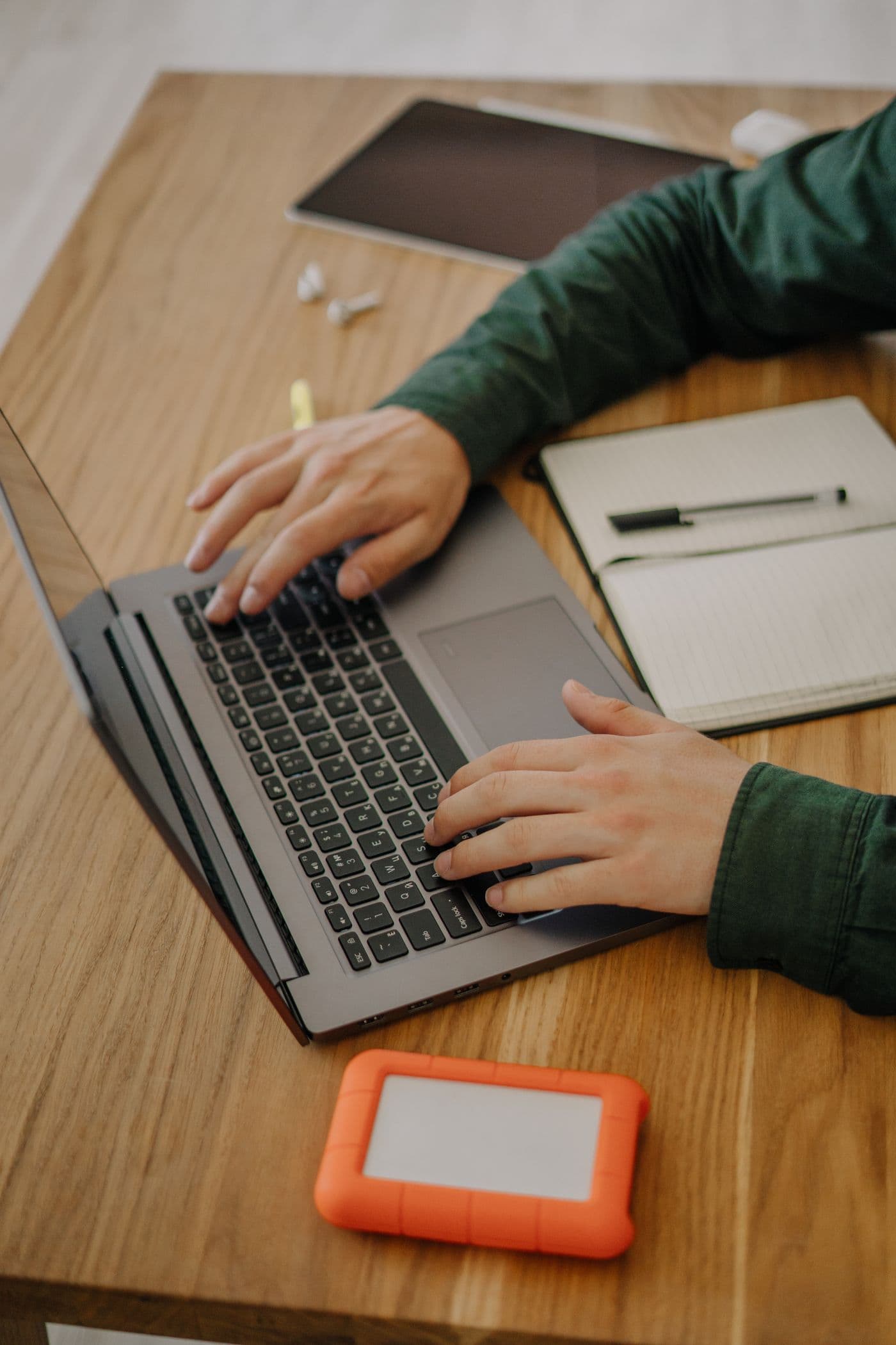 Hands working on a laptop beside an open notebook on a wooden desk